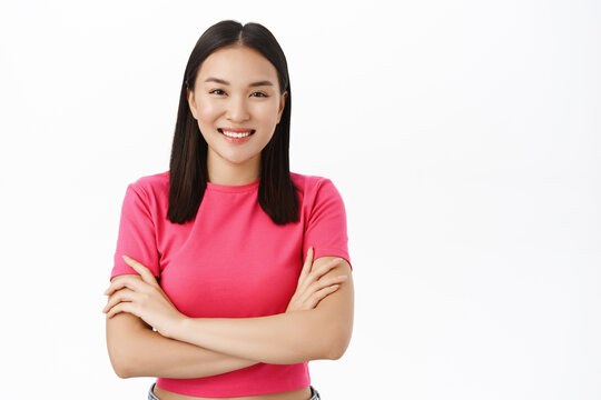 Close up of asian woman cross arms on chest, smiles and looks confident, stands over white background