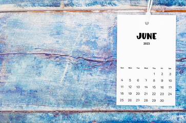The June 2023 calendar page hanged with white rope on old blue wooden background.