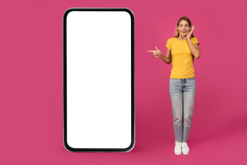 Shocked glad mature european blonde woman pointing finger at huge phone with empty screen