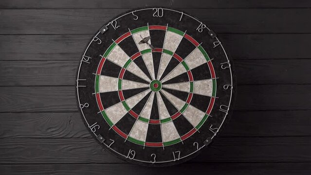 Three darts are aimed and thrown by hand and hit the dartboard on a black wooden background. Unlucky - none of the darts hit the bull's eye. The concept of loss and failure