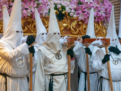 Nazarenos con t&uacute;nicas y capirotes blancos llevan sobre sus hombros un trono adornado con lirios rosas durante una emotiva procesi&oacute;n de Semana Santa en Espa&ntilde;a Murcia