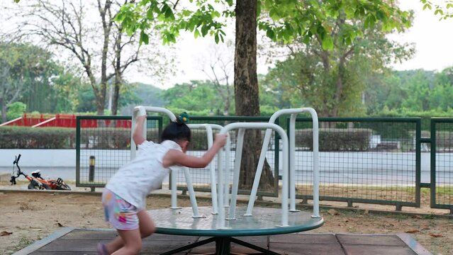 Cute little girl playing roundabout at playground.