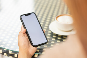 Illustration of woman's hand holding white mobile phone with blank screen and cup of coffee in cafe.