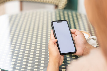 Illustration of woman's hand holding white mobile phone with blank screen and cup of coffee in cafe.