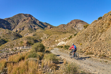 Obraz premium nice senior woman cycling with her electric mountain bike in the volcanic nature park of Cabo de Gata, Costa del Sol, Andalusia, Spain