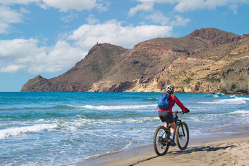 nice senior woman cycling with her electric mountain bike in the volcanic nature park of Cabo de Gata, Costa del Sol, Andalusia, Spain