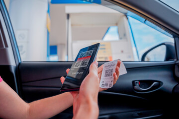 Woman using contactless payment by mobile phone with QR code at car filling station