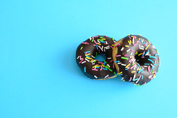 Two chocolate donuts with sprinkles on a blue background isolated, copy space 