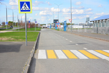 A road with a sign and white and yellow stripes of crossing in the city  