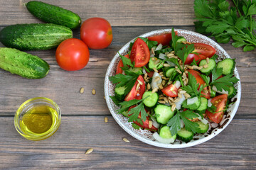 A bowl of cucumber and tomato salad with a glass of olive oil next to it 