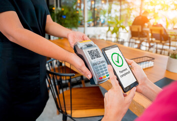 Woman using contactless payment by mobile phone with QR code at cafe
