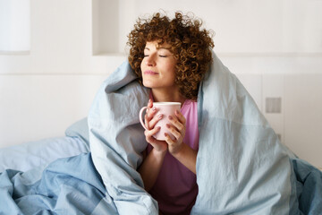 Dreamy lady drinking tea on bed