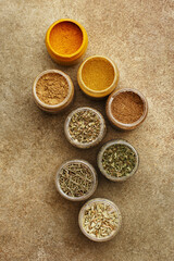 Various colorful spices in small jars on beige concrete background. Overhead view, close up