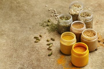 Various colorful spices in small jars on beige concrete background. Side view, close up