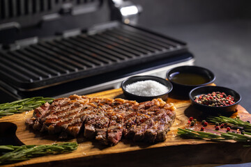 ribeye steak on wooden board with spices and electric grill