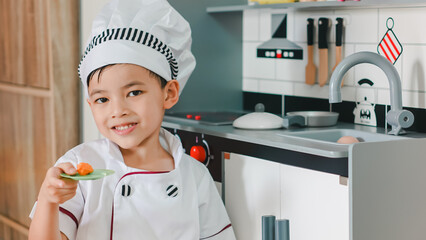 Little boy in chef hat and apron cooking in toy kitchen. Educational toys for young children. Kids play, portrait of Cute little Asian.playing at kitchen at indoor playground
