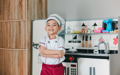 Little boy in chef hat and apron cooking in toy kitchen. Educational toys for young children. Kids...