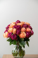 A large arrangement with peach and purple roses in a vase