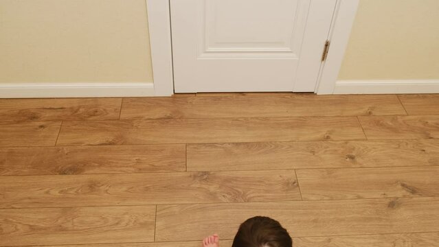 Funny baby crawls backwards while sitting on the floor. Child moves unusually on the floor in the home living room. Kid about two years old (age one year nine months)