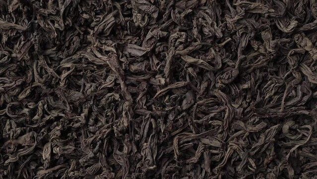 Background of black loose-leaf tea slowly rotating. Close up, top view