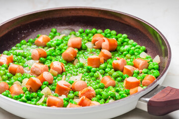 mixture of green peas with sausage in frying pan