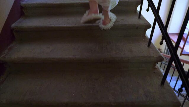 Bride in white wedding dress and funny fur slippers climb up stone stairs in a staircase.
