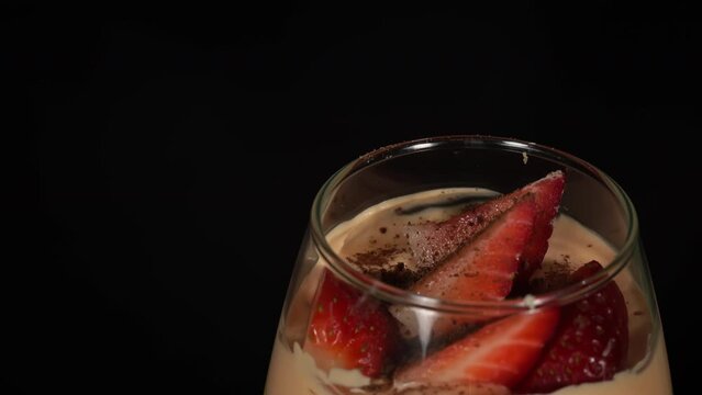 Trifle in glass with strawberries is spinning with beautiful decor. Pastry chef decorates fruit trifle for the holiday. Cake in a glass with different layers. Delicious dessert is spinning on a plate.