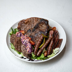 Grilled meat and sausages with herbs and vegetables on white plate. Meat plate. Barbecue menu. Top view. White background. Copy space. 