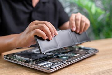 Laptop basic service of battery replacement, Technician Man holding the new battery and insert in...
