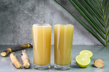 Sugarcane juice in glass cups with sugarcane, lemon and ginger in the background.