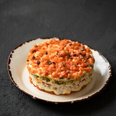 Layered salad with salmon, seasoned with mayonnaise. Serving of round salad on plate. Dark gray background. Side view. Copy space. High quality photo