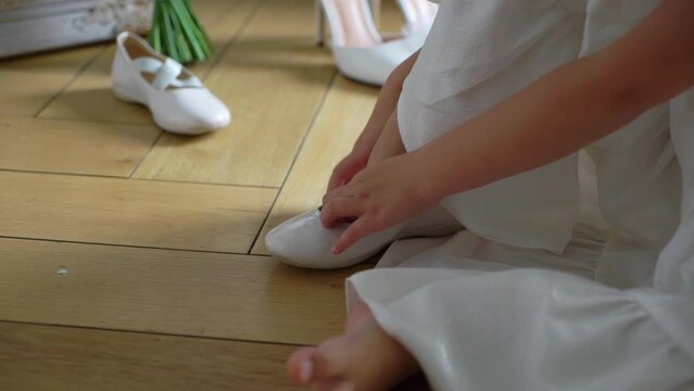 Young girl wear women's ballet flats. Daughter or bridesmaid. The bride in a white luxurious wedding dress puts on shoes.