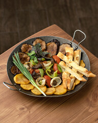 Fried vegetables with pita bread and green onions in metal brazier. Baked eggplant, tomatoes, peppers, potatoes. Wooden background. View from above. Copy space. 