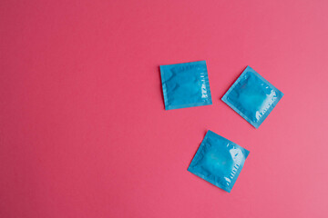 Lots of blue packages of unopened condoms on a pink background. Condom use reduces the likelihood...