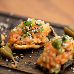 Snacks with red fish paste are decorated with green onions and sesame seeds on wooden board. Cold appetizers. Sandwiches with salmon. Side view. Soft focus. Close-up. 