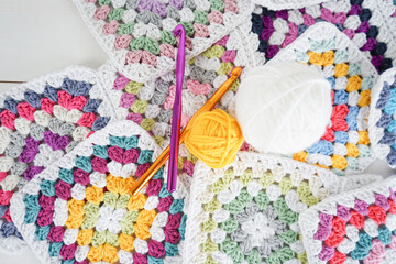colorful woolen balls with multicolored granny squares and crochet hooks on white wooden ground