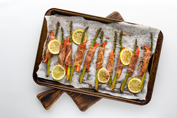 A sheet pan topped with prosciutto wrapped asparagus spears on a wooden board.