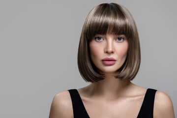 Portrait of beautiful fashion woman with bob hairstyle. Thick short wig. Gray background