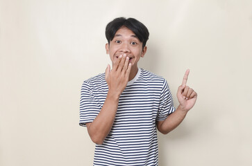 Asian man on isolated background pointing up and doing silent gesture