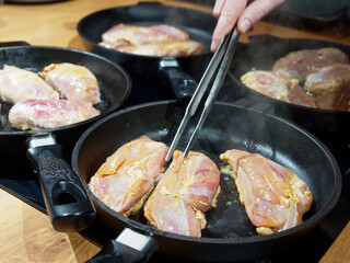 Chicken fillet fried in four pans and hand with tweezers in the foreground