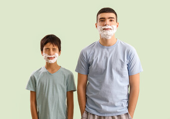 Man and his little son with shaving foam on faces against light color background
