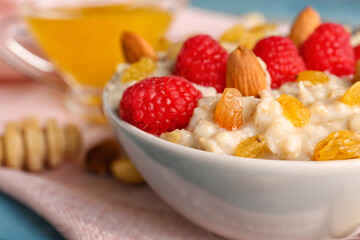 Bowl with tasty oatmeal, raspberries, nuts and raisins on blue wooden background