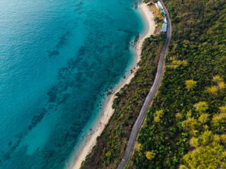 Aerial view of an idyllic sea sandy beach with asphalt winding road and small car driving on. Background for travel and vacation
