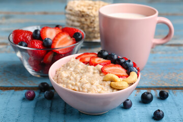 Bowl with tasty oatmeal, strawberries, blueberries and cashew on blue wooden background