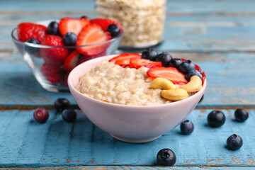 Bowl with tasty oatmeal, strawberries, blueberries and cashew on blue wooden background