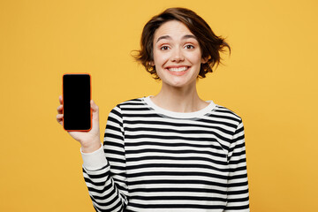 Young woman wear casual striped black and white shirt hold in hand use mobile cell phone with blank screen workspace area isolated on plain yellow color background studio portrait. Lifestyle concept.