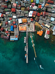 Fototapeta na wymiar A bird's eye view of a ship navigating fishing boats moored to the docks, with village houses sprawling between the harbor 