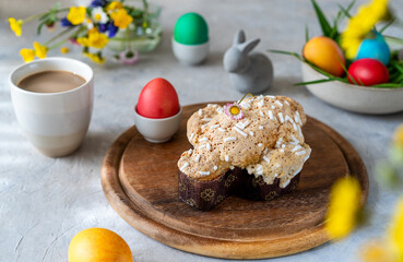 Italian Easter cake Colomba on wooden cutting board with painted eggs, easter decoration, mug of coffee and wild flowers