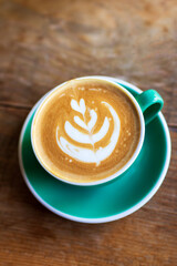 Cup of coffee with latte art on wooden table with morning sunlight through from window. Beautiful morning.