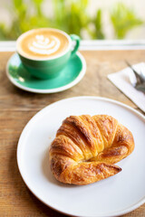 Cup of coffee with latte art with croissants on wooden table and morning sunlight with shadow through from window. Beautiful meal with warm sunlight.